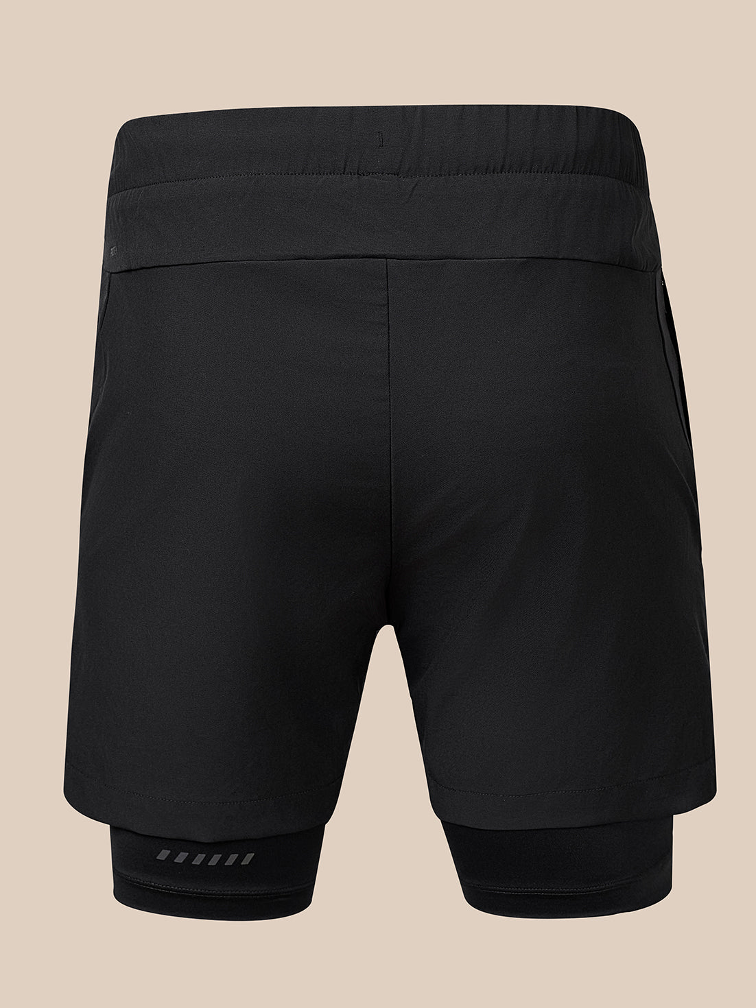 Black athletic compression shorts with an integrated inner layer, shown from the back on a solid beige background.