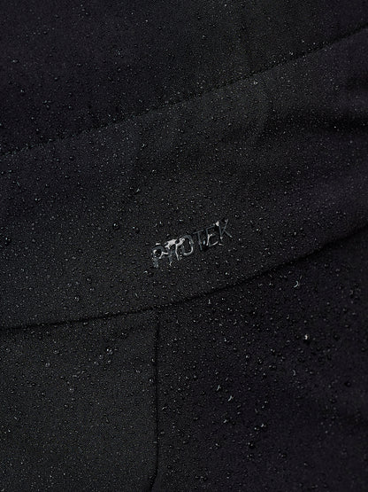 Close-up of a black waterproof fabric with water droplets beaded on the surface and a small metallic 'PROTEK' logo embossed on the seam.