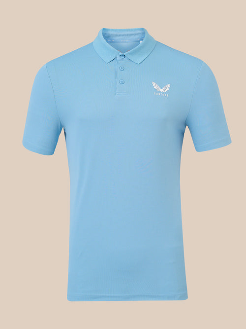 A light blue short-sleeve polo shirt with a three-button placket and a small white wing logo on the left chest, displayed on a solid beige background.