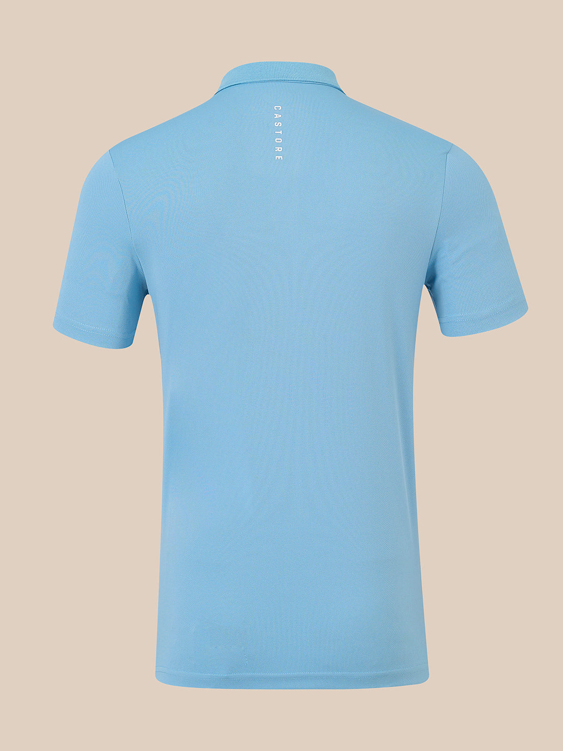 A light blue short-sleeve polo shirt shown from the back, featuring a vertical 'CASTORE' logo printed in white near the collar, set against a solid beige background.
