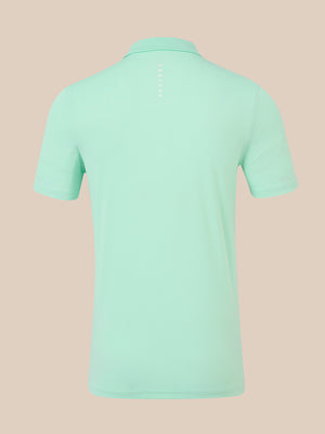 A mint green short-sleeve polo shirt shown from the back, featuring a vertical white 'CASTORE' logo printed on the upper back, set against a solid pale peach background.