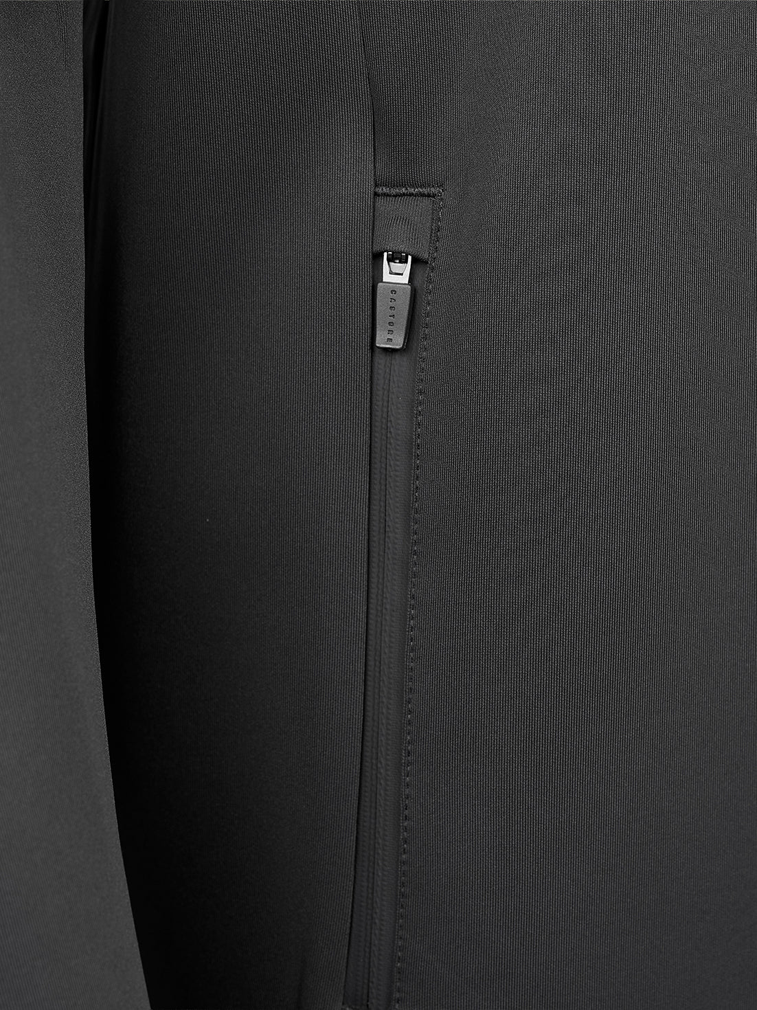 Close-up of a black zippered pocket on a dark gray or black fabric garment, showing the zipper pull and stitching details.