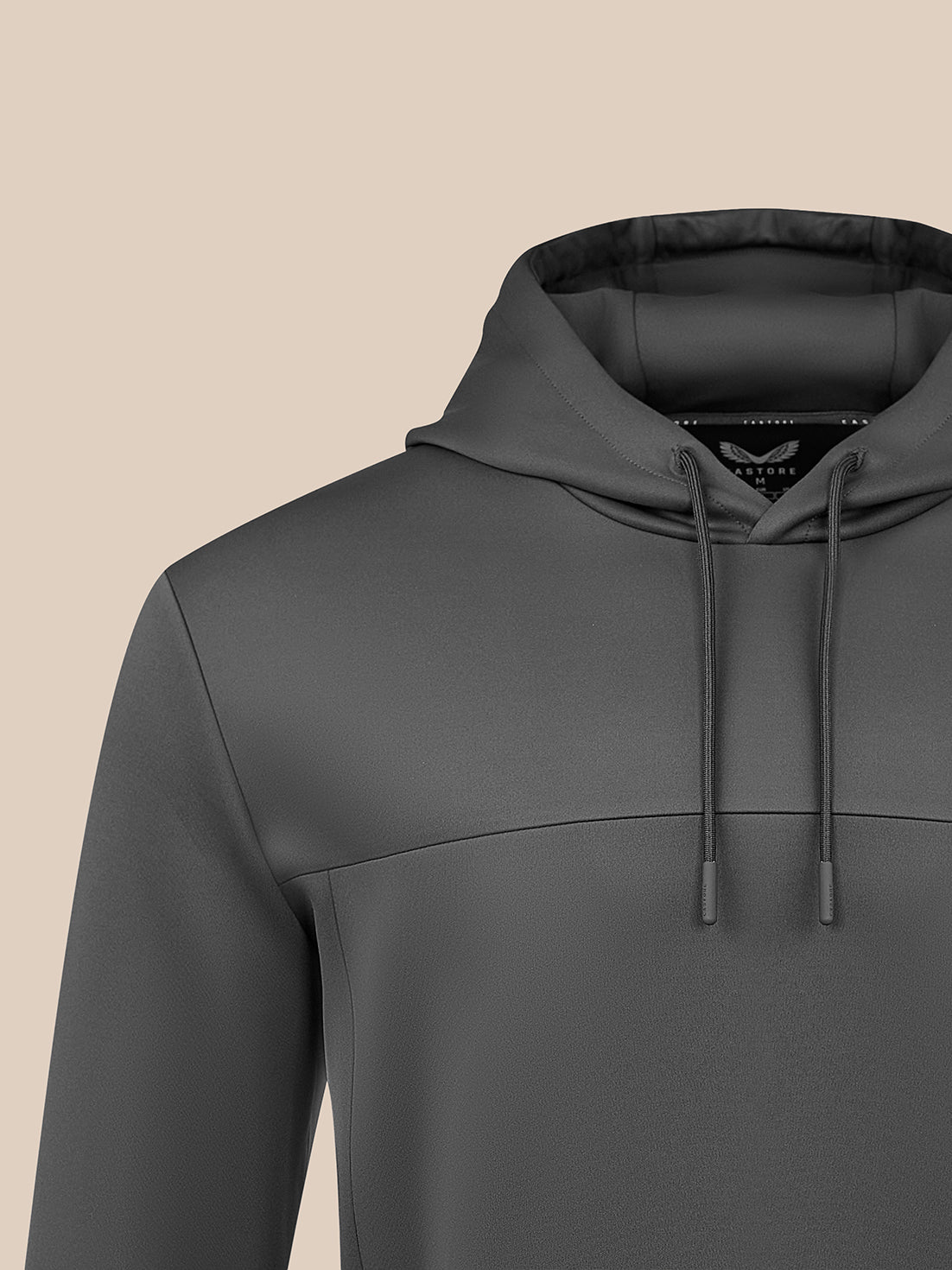 A close-up of a dark gray hooded sweatshirt with matching drawstrings, shown against a solid beige background.