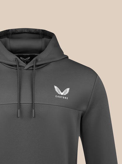 A dark gray pullover hoodie with a white winged logo and the word 'CASTORE' on the left chest, shown against a solid beige background.