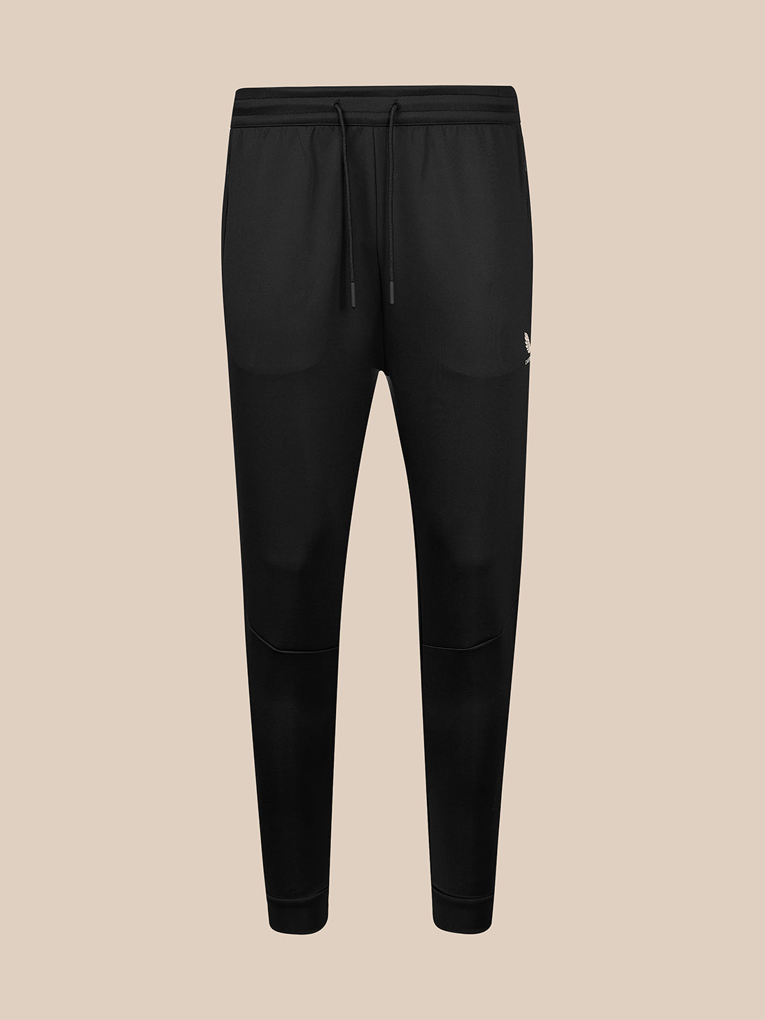 Black jogger-style sweatpants with an elastic waistband, black drawstring, and a small white logo on the left hip, shown against a solid beige background.