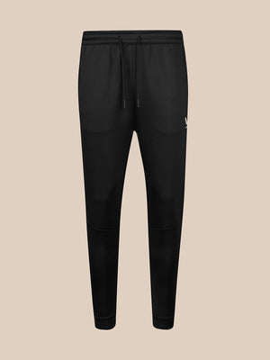 Black jogger-style sweatpants with an elastic waistband, black drawstring, and a small white logo on the left hip, shown against a solid beige background.