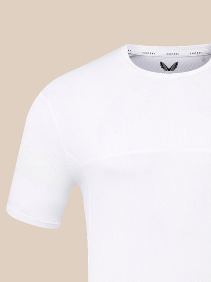 A close-up of a white short-sleeve crewneck athletic t-shirt by CASTORE, showing the textured fabric and the black wing logo on the inner neck label, set against a solid beige background.