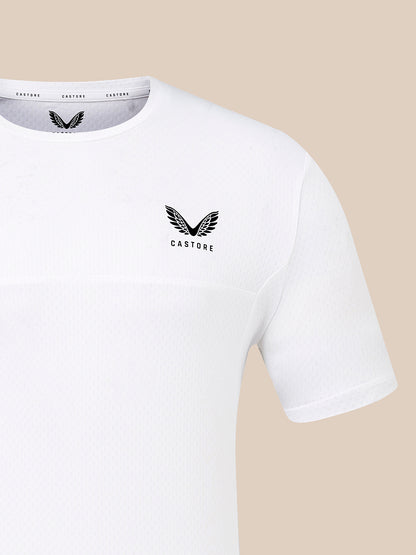 A close-up of a white short-sleeve athletic t-shirt with a black winged logo and the word 'CASTORE' printed on the left chest, set against a solid beige background.