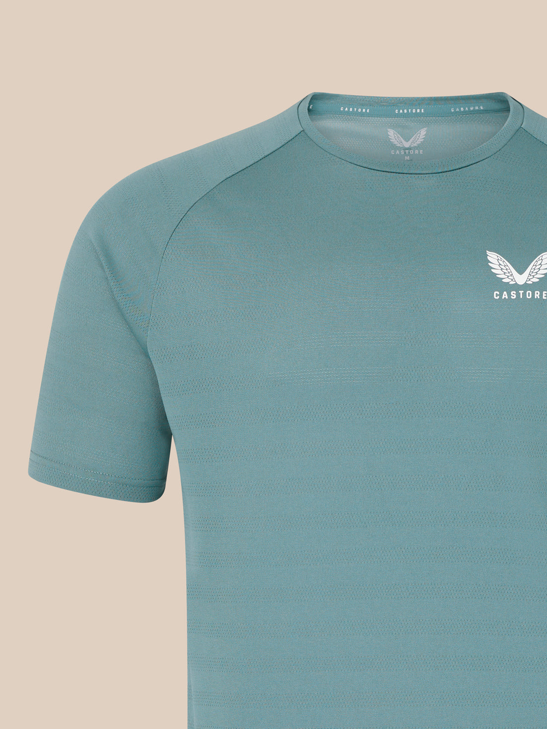 Close up of teal blue men's short sleeve performance T shirt with subtle knit texture and white Castore wing logo on the chest.