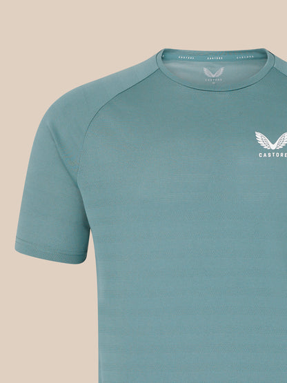Close up of teal blue men's short sleeve performance T shirt with subtle knit texture and white Castore wing logo on the chest.