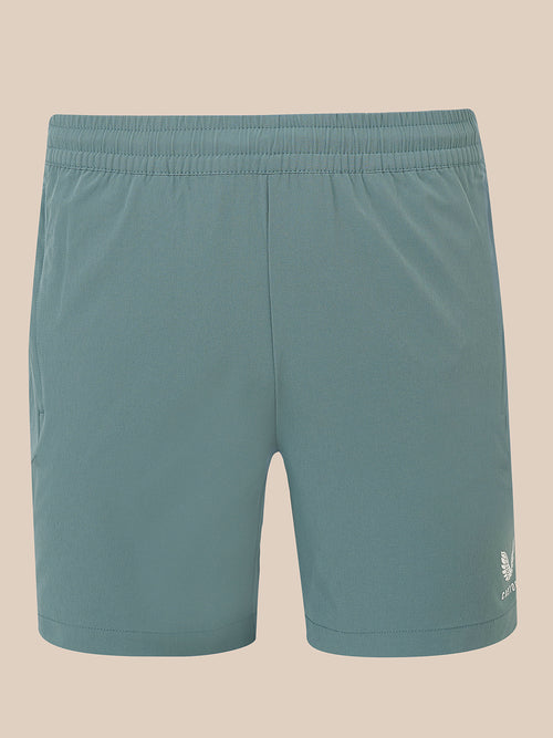 A pair of men's athletic shorts in a muted teal-blue color, featuring an elastic waistband and a small white embroidered logo on the lower left hem, displayed against a solid beige background.