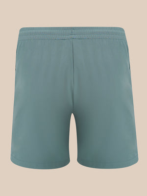 A pair of solid teal-blue athletic shorts with an elastic waistband, shown from the back against a solid beige background.