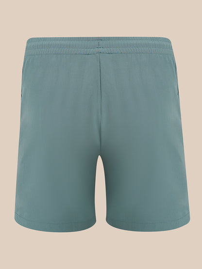 A pair of solid teal-blue athletic shorts with an elastic waistband, shown from the back against a solid beige background.