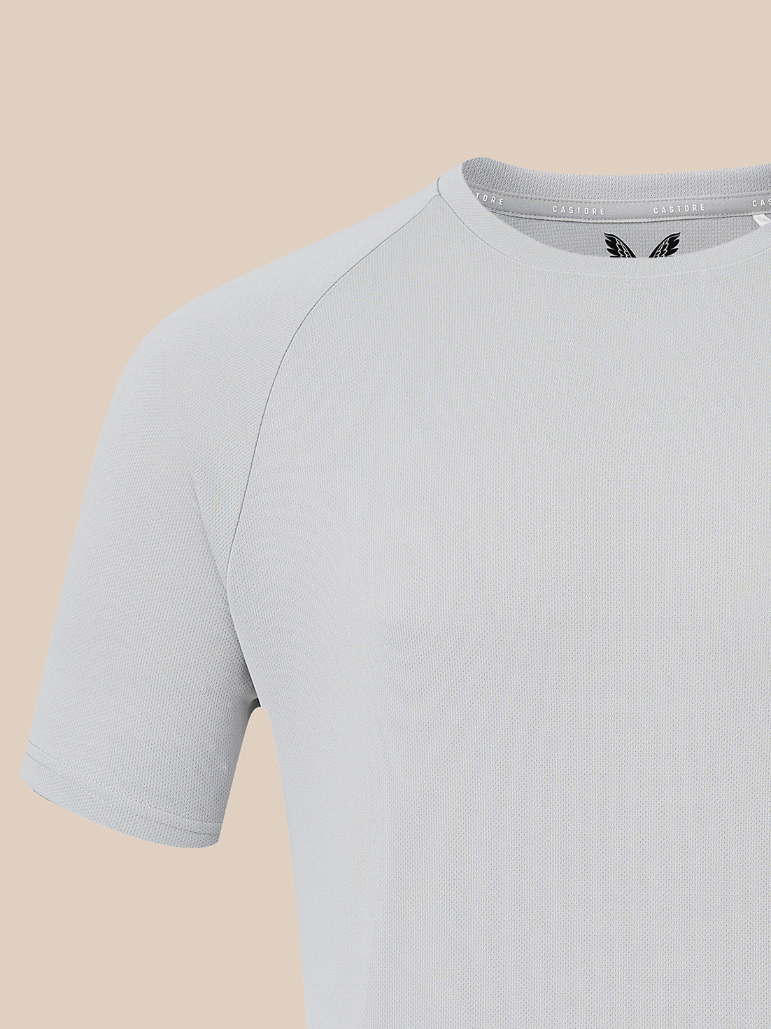 A close-up of a light gray short-sleeve athletic t-shirt with raglan sleeves, shown against a solid beige background.