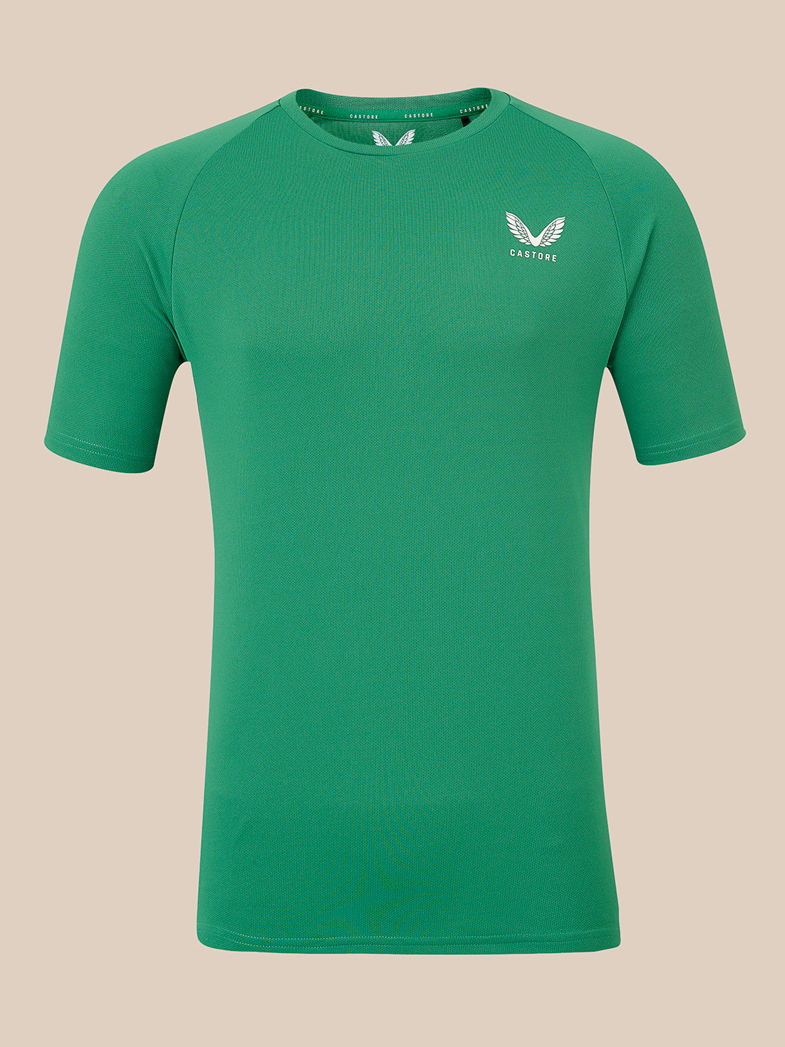 A green short-sleeve athletic t-shirt with a white winged logo on the left chest reading 'CASTORE', displayed against a solid beige background.