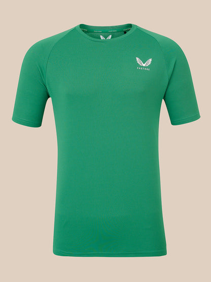 A green short-sleeve athletic t-shirt with a white winged logo on the left chest reading 'CASTORE', displayed against a solid beige background.