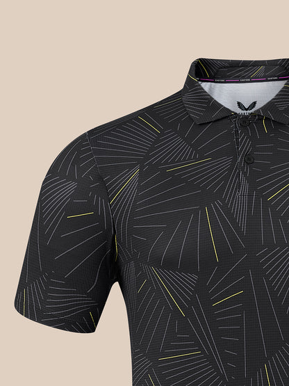 A close-up of a short-sleeve polo shirt with a black base and an abstract geometric line pattern in white and yellow, shown against a solid beige background.