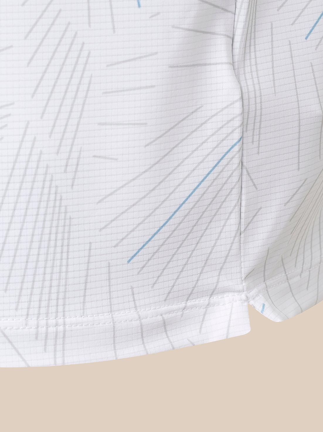 Close-up of a white fabric garment with a fine gray grid pattern and scattered thin blue line accents, shown against a light beige background.