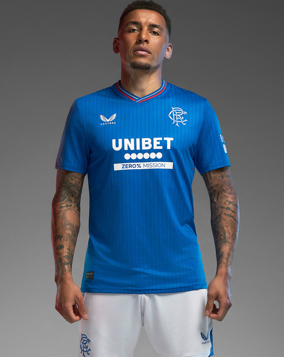 Full-body view of a model wearing the Rangers 23/24 blue home shirt with UNIBET sponsor and white shorts.