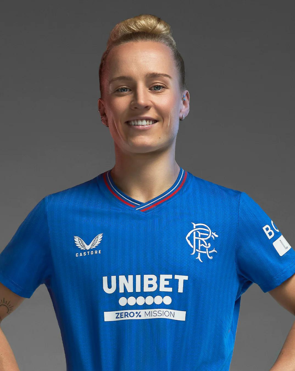Smiling model wearing blue Rangers Women's 23/24 home shirt with crest and sponsor on the front.