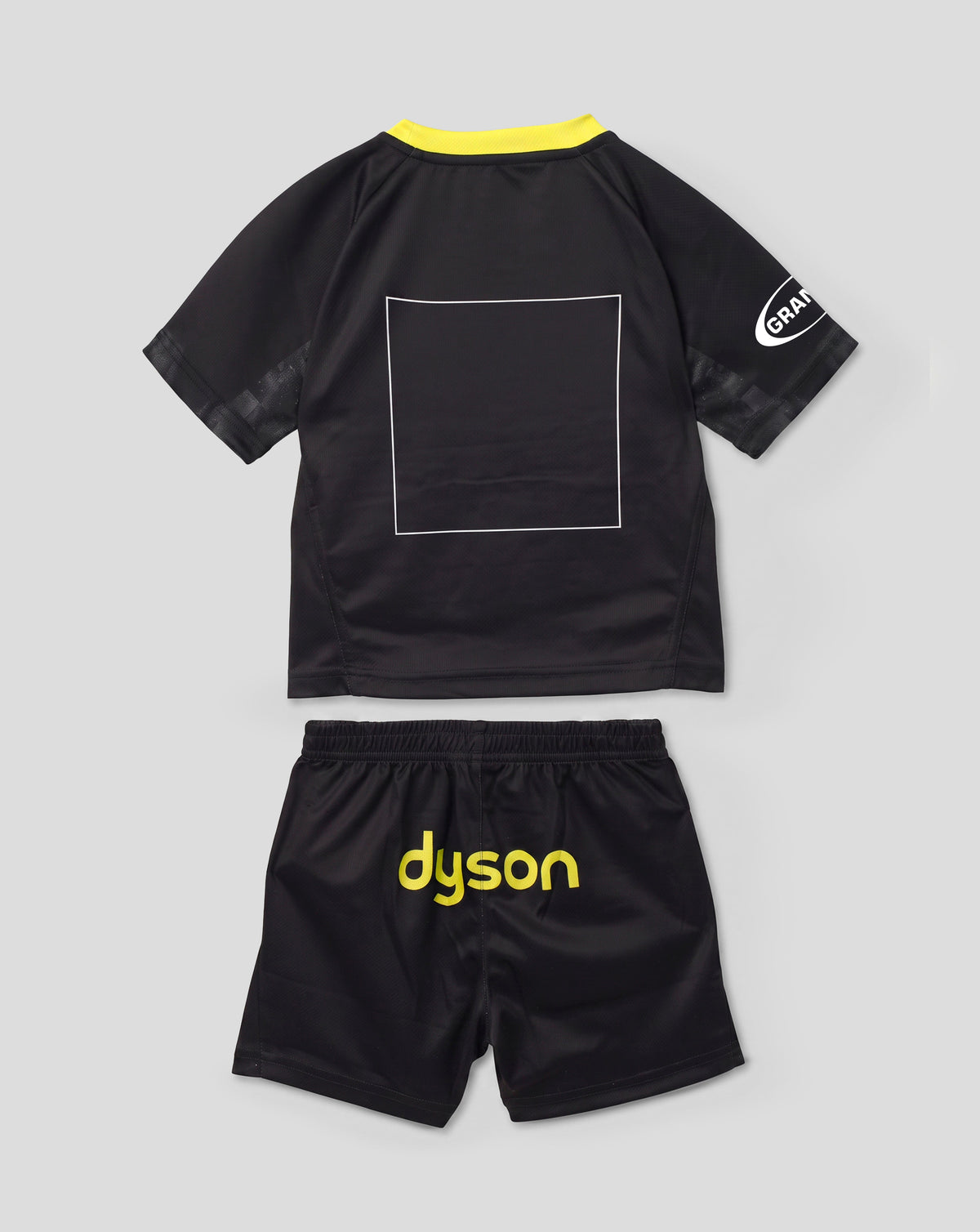 A toddler black short-sleeve jersey and matching shorts set from Dyson, shown flat-laid on a light gray background. The jersey features a bright yellow collar, a white outlined square on the back, and a white circular logo on the sleeve.