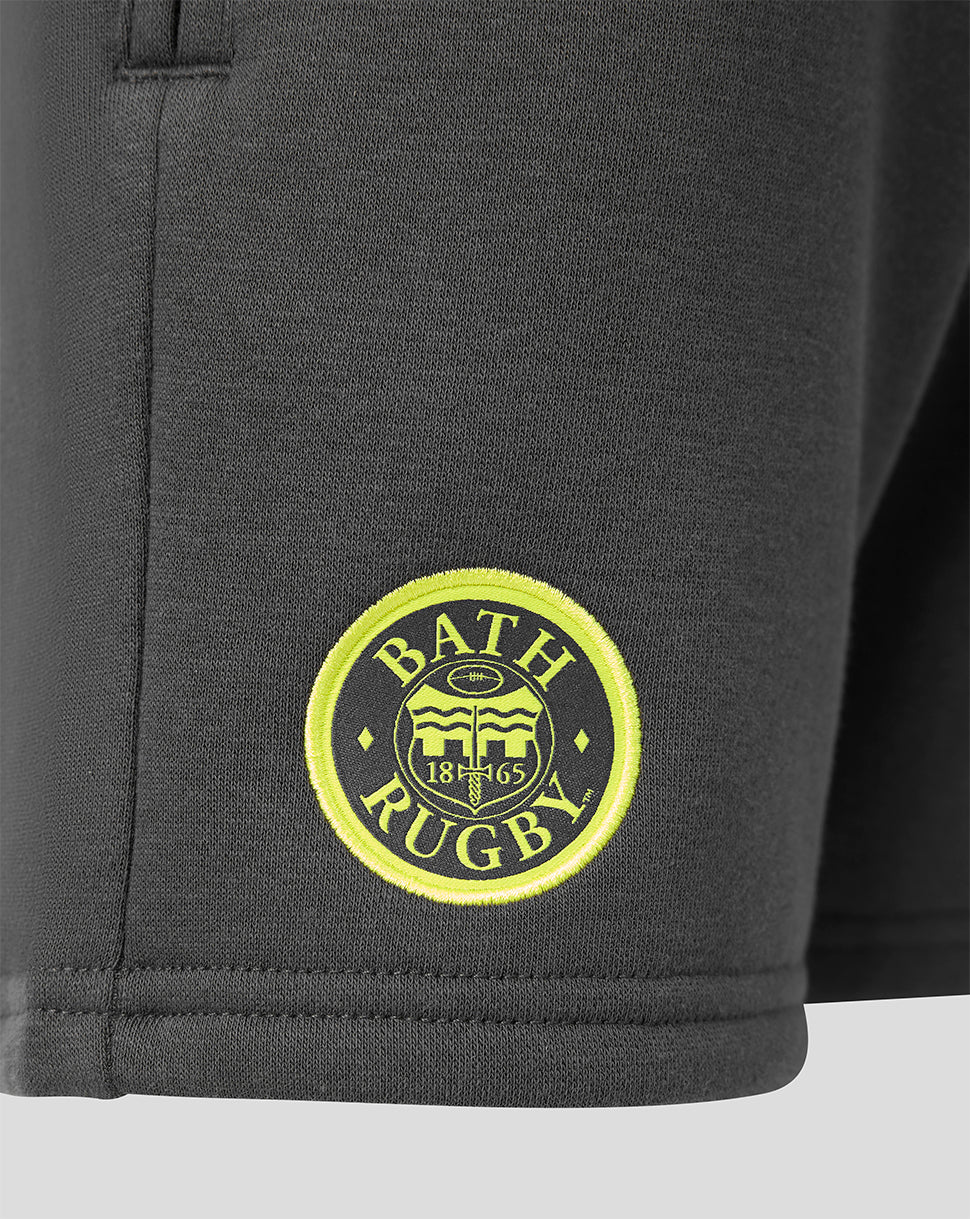 Close-up of dark gray athletic shorts with a circular yellow and black Bath Rugby embroidered patch on the lower left leg.