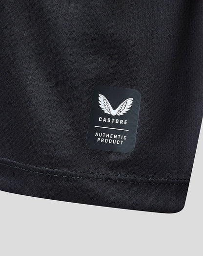 Close-up of a black athletic garment showing a sewn-on Castore Authentic Product label on the fabric, with a light gray background.