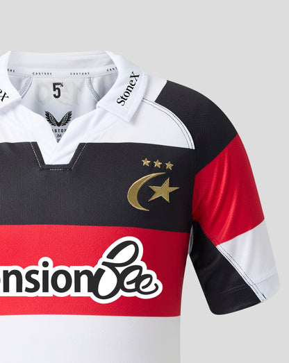 A close-up of a rugby jersey with a color-blocked design in white, black, and red, featuring a gold crescent and star logo with three stars on the chest. The collar displays 'StoneX' branding, and the front has a large 'nsionBe' sponsor logo.
