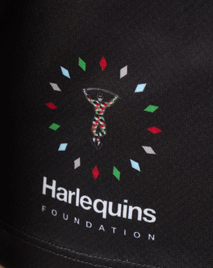 Close-up of a black fabric surface featuring a colorful embroidered or printed Harlequins Foundation logo with white text below.