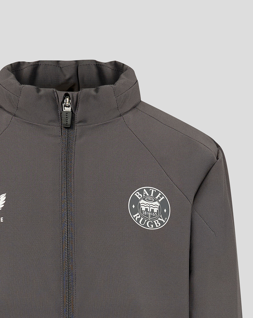 Close-up of a dark gray athletic zip-up jacket with a high collar, featuring a white circular Bath Rugby crest on the left chest and a partial white wing logo on the right chest, set against a light gray background.