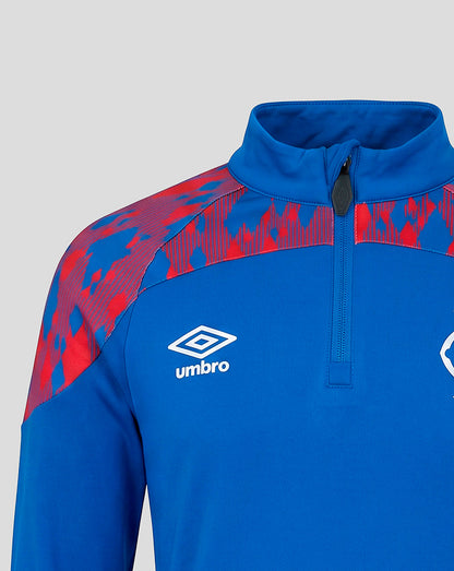A close-up of a blue and red patterned athletic quarter-zip jacket by Umbro, featuring a white embroidered logo on the chest, set against a neutral gray background.