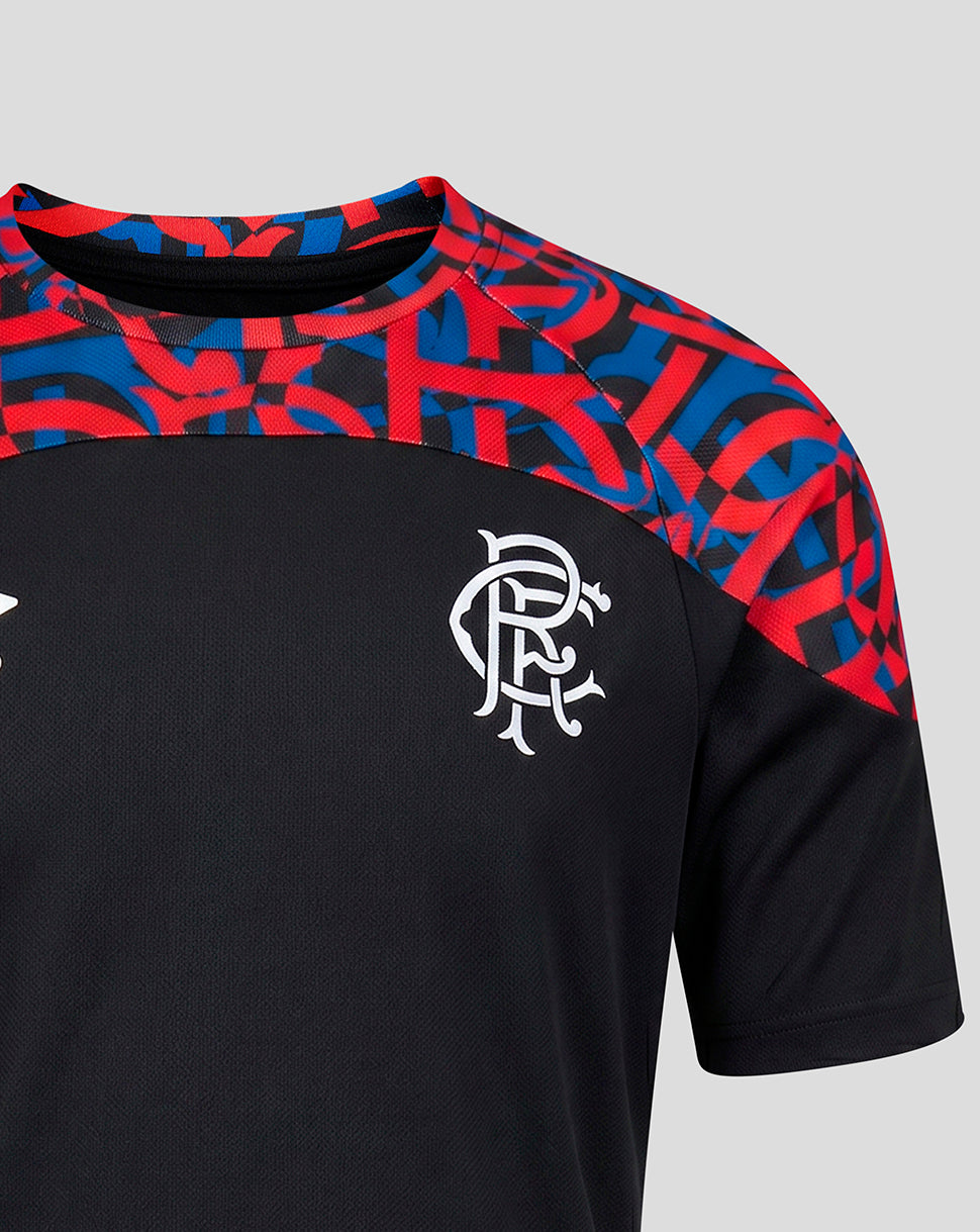 Close-up of a black short-sleeve sports jersey with a red and blue abstract patterned yoke and a white Rangers FC crest on the chest, shown against a light gray background.