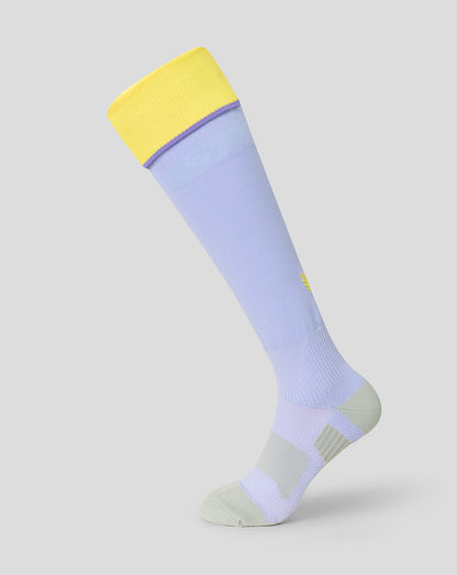 A close-up of a light periwinkle blue knit sock featuring a yellow embroidered wing logo on the upper calf, set against a solid light gray background.