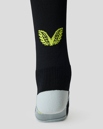 A close-up of a black athletic sock with a bright lime green butterfly graphic on the calf and a light gray toe section, shown against a neutral light gray background.