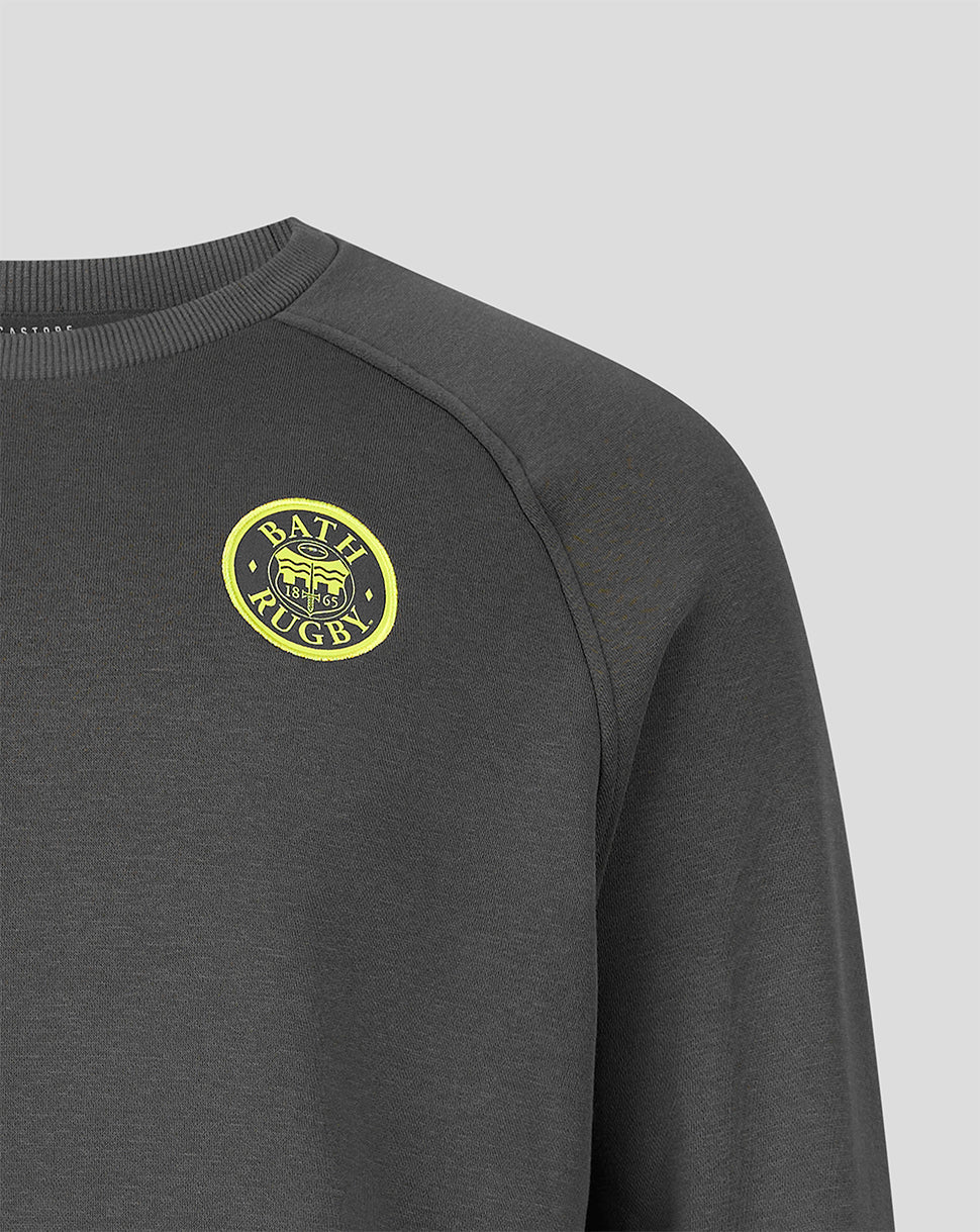Close-up of a dark gray crewneck sweatshirt featuring a yellow circular 'BATH Rugby' logo on the left chest, set against a light gray background.