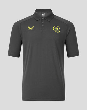 A dark gray short-sleeve polo shirt with a yellow Castore logo on the right chest and a yellow circular club crest on the left chest, displayed against a solid gray background.