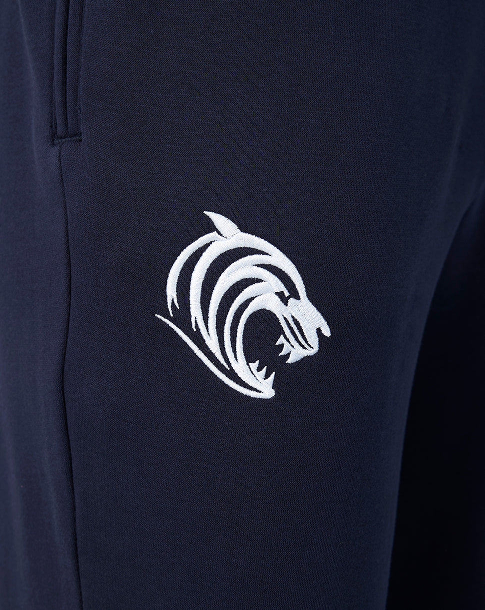 Close up of navy travel joggers fabric with a white embroidered tiger logo on the leg.