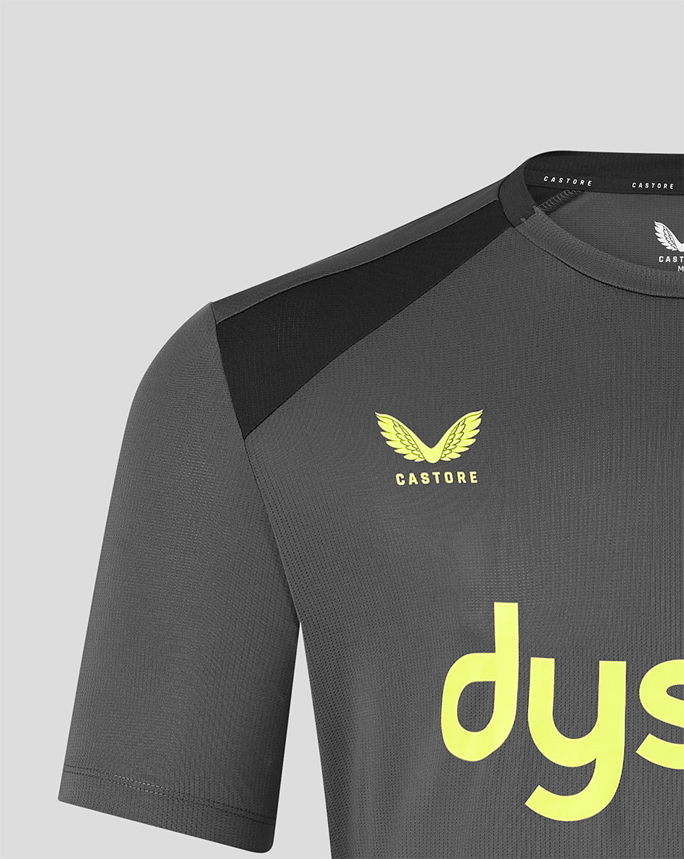 Close-up of a dark gray athletic jersey with a black shoulder panel, a yellow Castore wing logo on the chest, and a large yellow sponsor logo on the front, shown against a light gray background.
