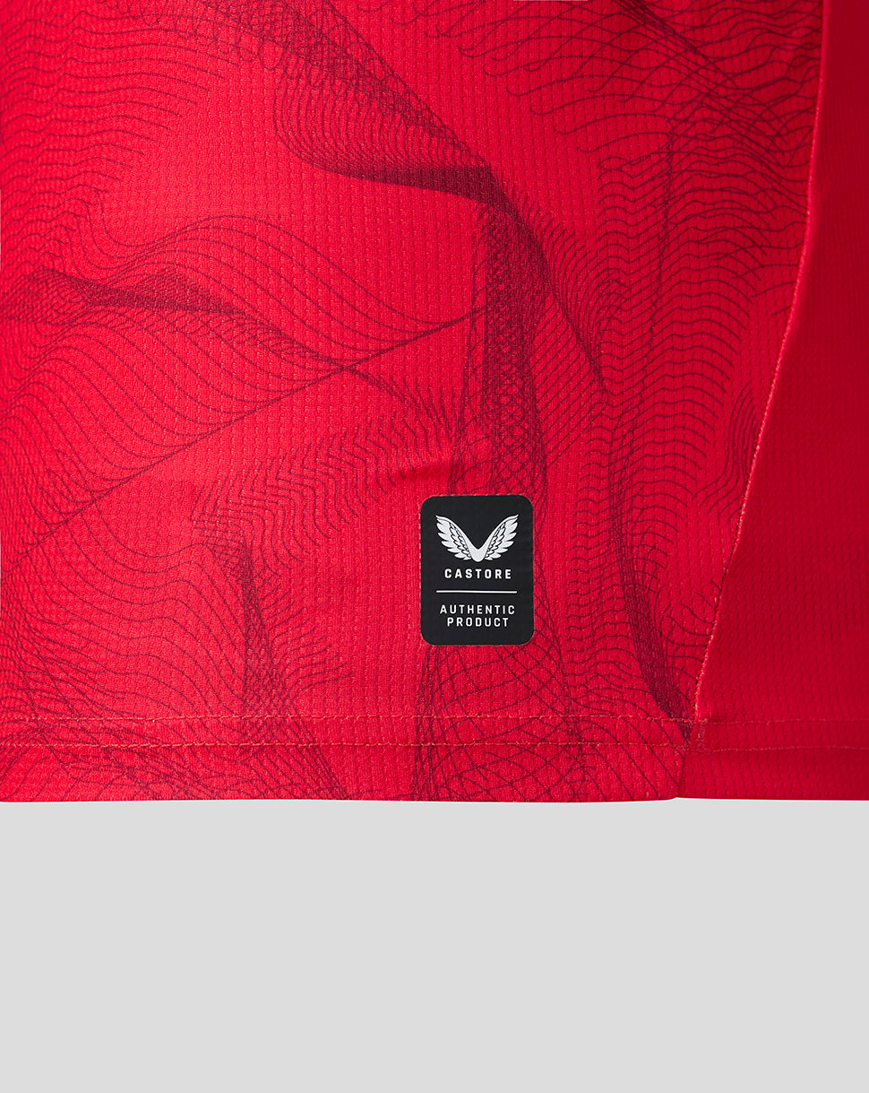 Close-up of a bright red athletic garment with a subtle wavy pattern and a black Castore Authentic Product label near the lower center.