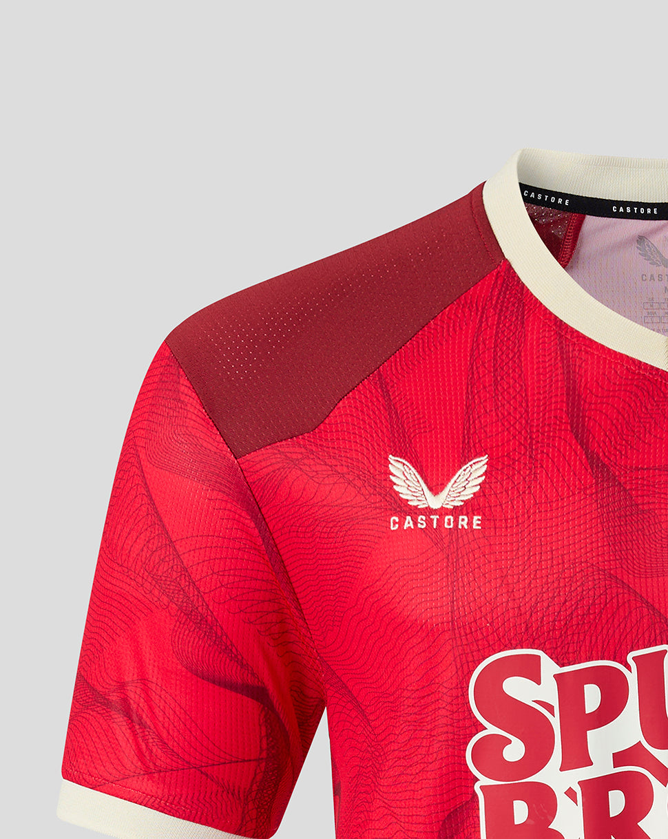 Close-up of a red Castorefootball jersey with a textured pattern, featuring a white wing logo and the brand name 'CASTORE' on the chest, set against a light gray background.