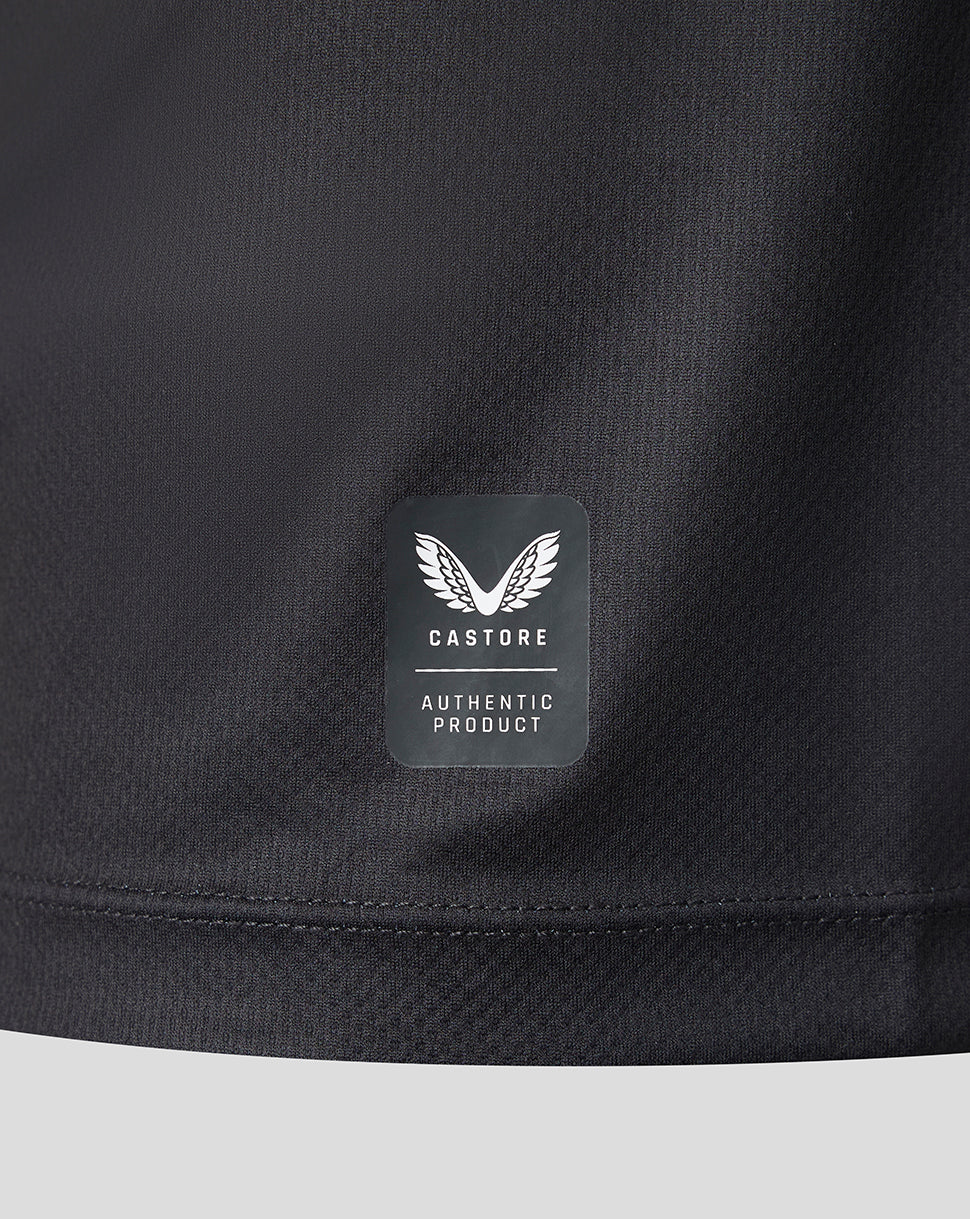 Close-up of a black athletic jacket or sweatshirt showing the lower hem and a rectangular Castore 'Authentic Product' logo patch on the chest.