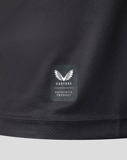 Close-up of a black athletic jacket or sweatshirt showing the lower hem and a rectangular Castore 'Authentic Product' logo patch on the chest.