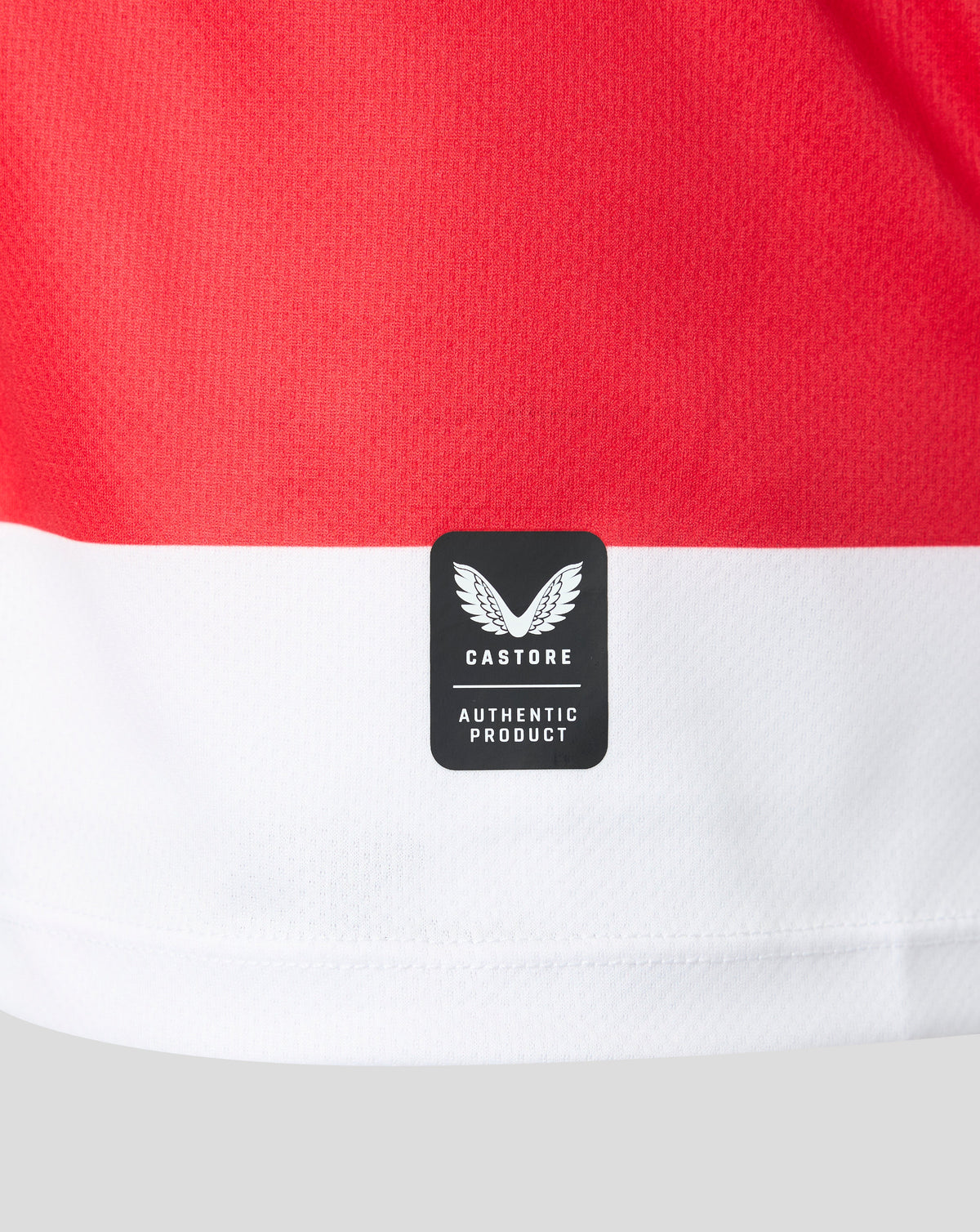 Close-up of a red and white striped athletic jersey with a black Castore Authentic Product patch on the front.