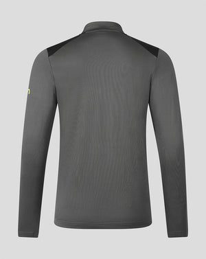 A dark gray long-sleeve athletic top shown from the back, featuring black shoulder panels and a small yellow logo on the left sleeve, set against a solid light gray background.