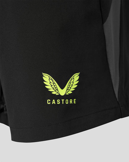 Close-up of a black athletic garment showing a bright yellow-green Castore wing logo and brand name printed on the lower front, with a dark side panel visible.