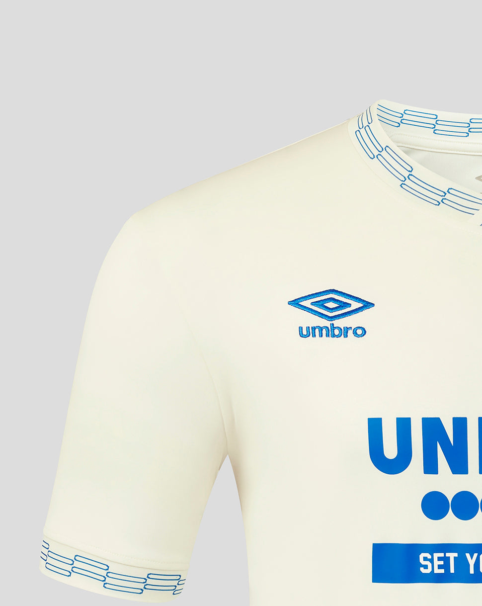 Beige sports jersey with blue accents and Umbro logo on a gray background