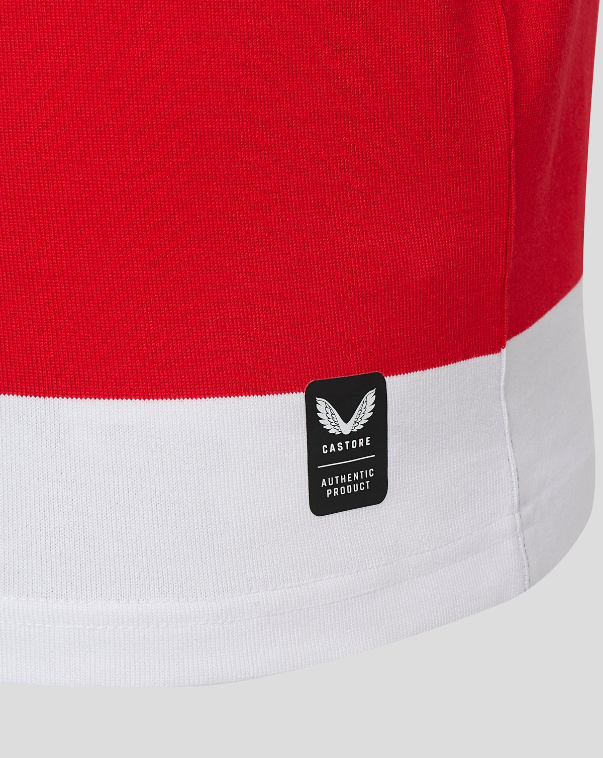 Close-up of a red and white color-blocked knit garment, showing a black Castore brand patch on the white hem.
