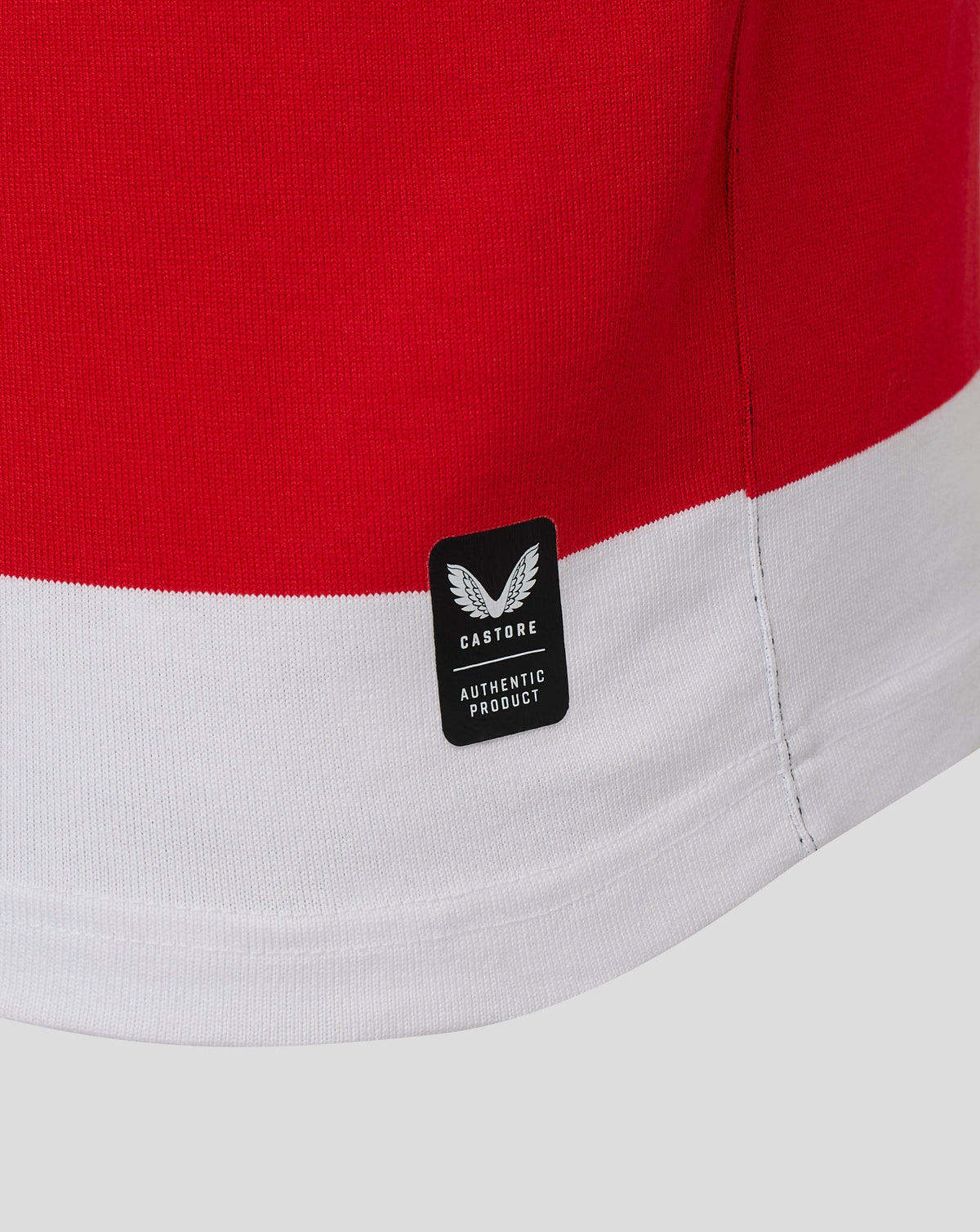 Close-up of a red and white striped garment, showing a black rectangular brand patch with a winged logo and the text 'CASTORE AUTHENTIC PRODUCT'.