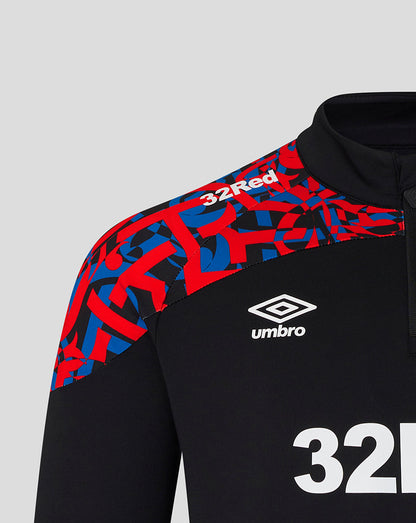 Close-up of a black athletic quarter-zip top with a red and blue geometric pattern across the right shoulder and upper chest, plus a white Umbro logo and the number 32.