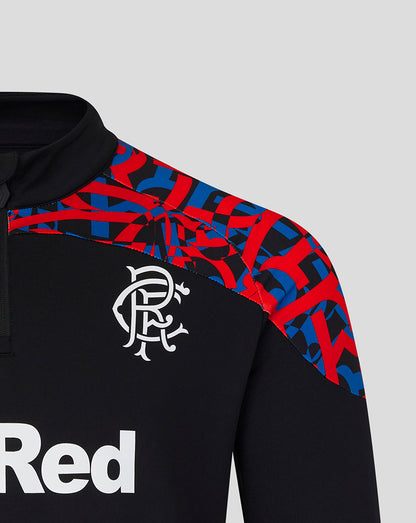 Close-up of a black long-sleeve sports top with a red and blue geometric pattern across the shoulders and upper chest, a white Rangers FC crest on the chest, and part of a white 'Red' sponsor logo on the front, set against a light gray background.